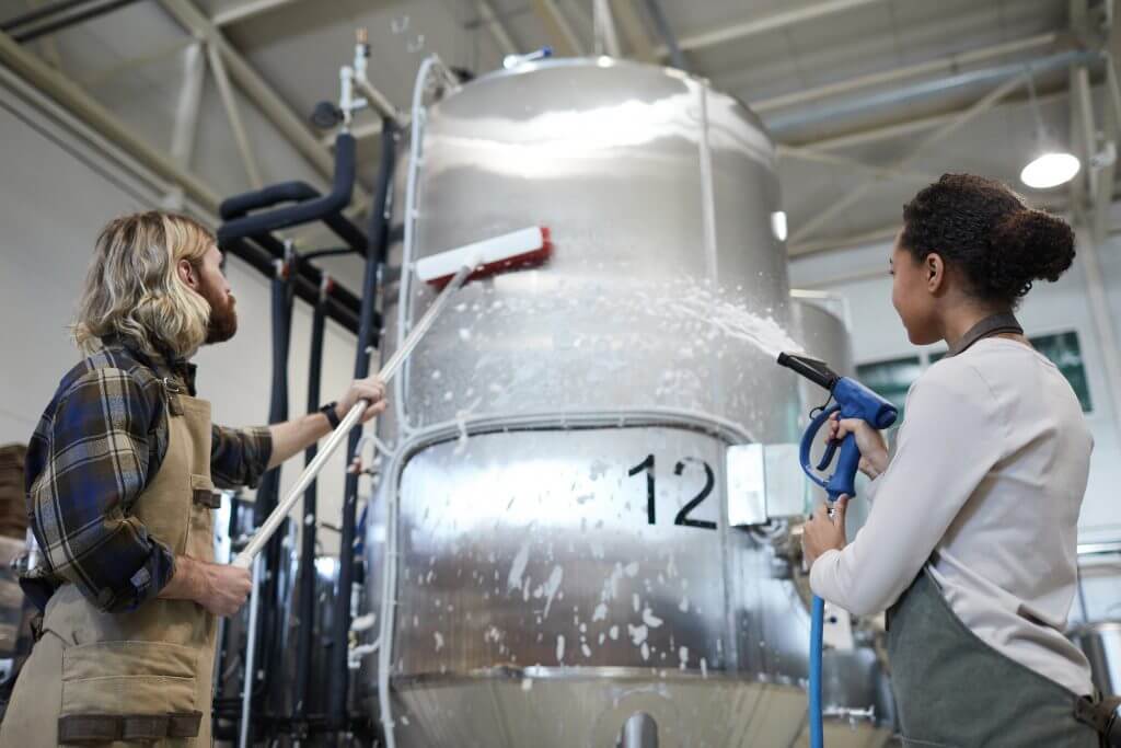 Low angle view at two workers washing equipment at modern industrial brewery